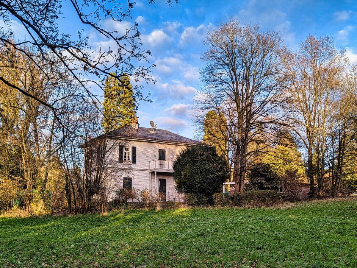 Historisches Schindelhaus inmitten der Rosenhöhe, umgeben von Bäumen und Grünflächen.