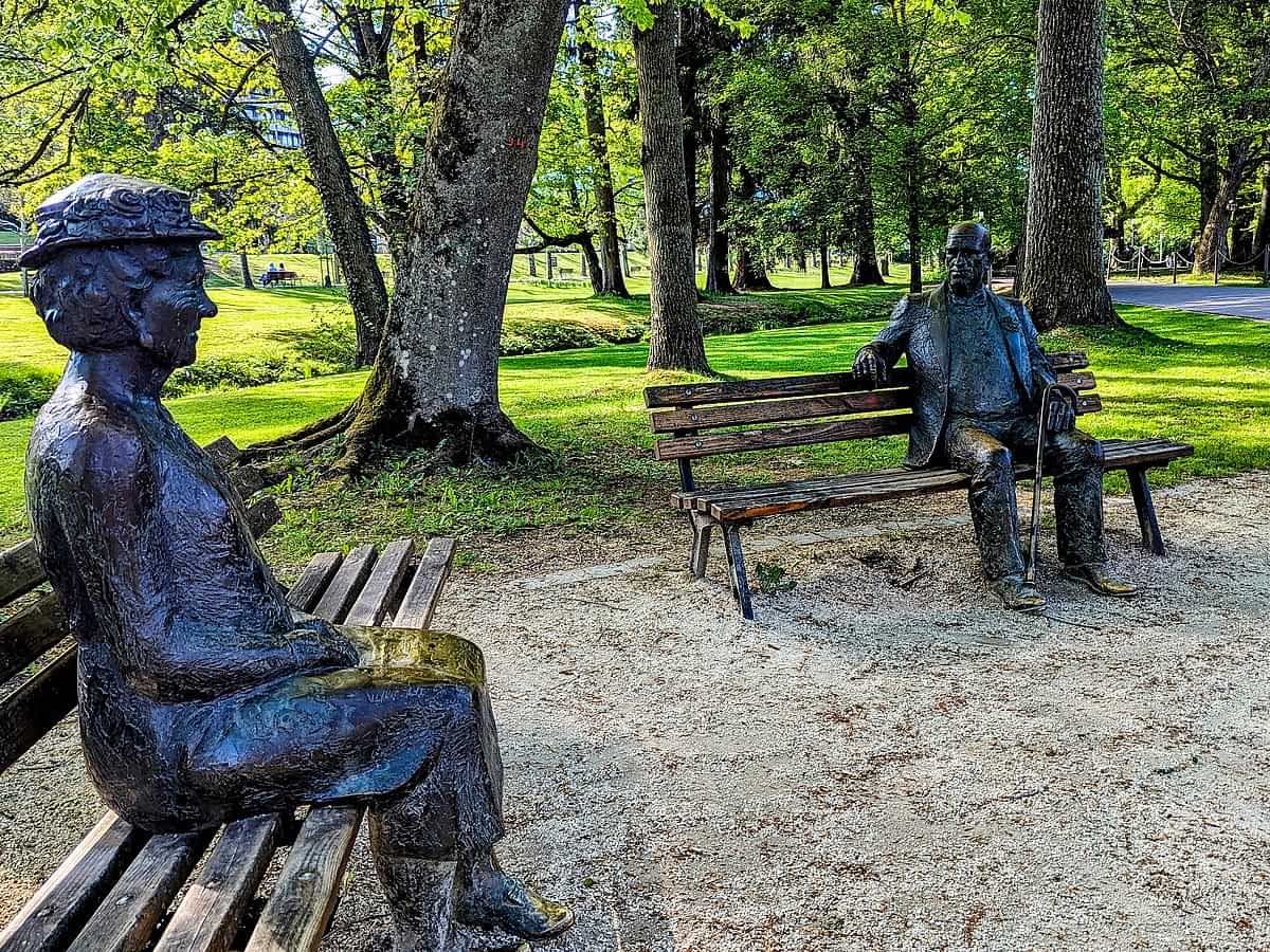 Kurpark Bad Orb mit Bronzestatuen auf Bänken unter alten Bäumen