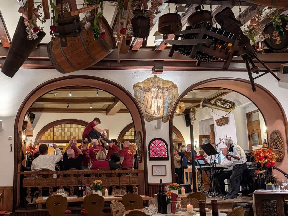 Blick in den gemütlichen Gastraum des Rüdesheimer Schlösschens mit rustikaler Deckendekoration, einer Live-Band und fröhlichen Gästen beim Feiern
