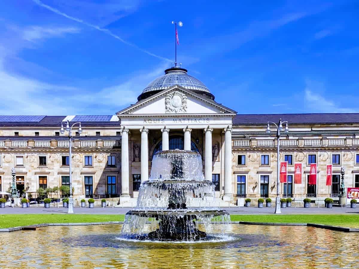 Frontansicht des klassischen Kurhauses Wiesbaden mit großen Säulen, Kuppel und einem sprudelnden Springbrunnen im Vordergrund