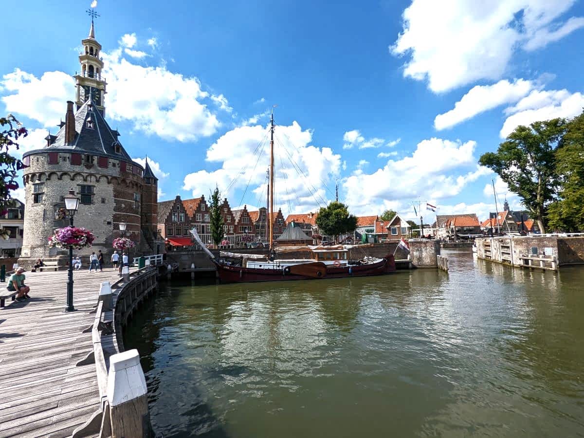 Blick auf den Hafen von Hoorn mit dem historischen Hoofdtoren, einem alten Segelschiff am Kai und typisch niederländischen Giebelhäusern im Hintergrund.