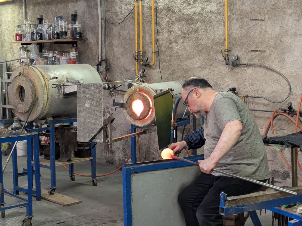 Ein Glasbläser in seiner Werkstatt in Kaysersberg bei der Arbeit mit glühendem Glas vor einem Schmelzofen.