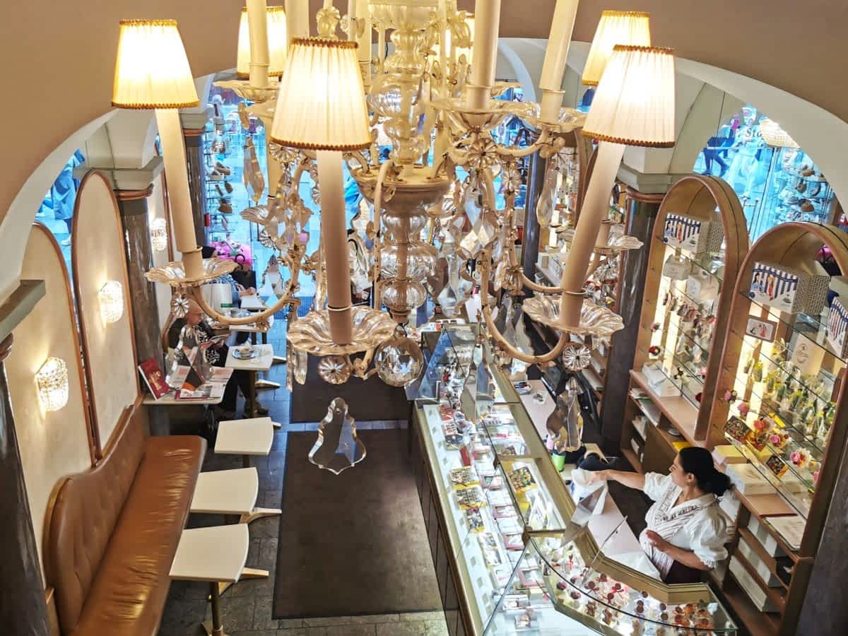 Blick von oben in ein elegantes Wiener Kaffeehaus mit einem großen, prunkvollen Kronleuchter und Kuchentheke