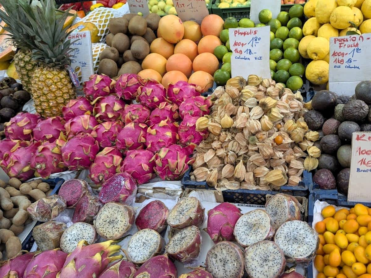 Bunter Obststand am Wiener Naschmarkt mit einer Auswahl an exotischen Früchten wie Drachenfrüchten, Physalis, Zitronen und Kumquats inklusive Preisschildern